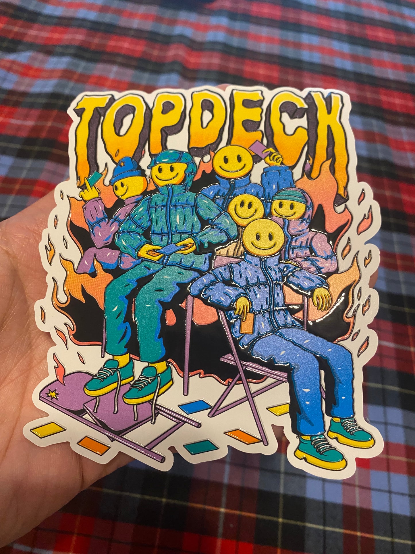 TopDeck.gg Smiley Squad embossed sticker featuring cartoon characters in blue outfits with yellow smiley faces sitting in chairs surrounded by flames.