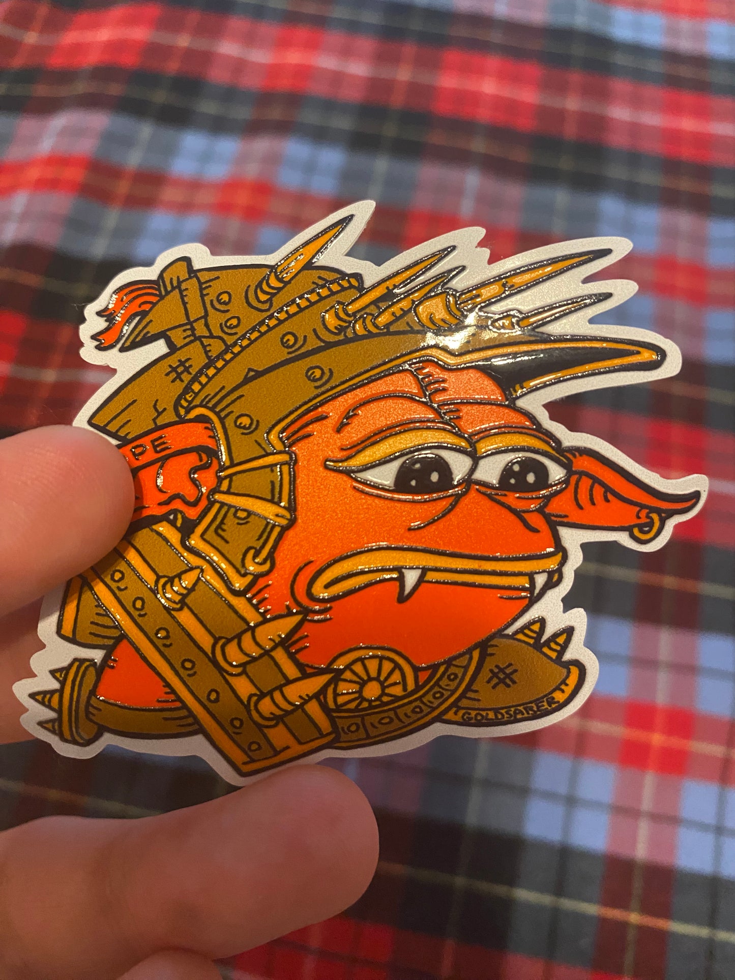 TopDeck.gg Sad Rograkh embossed sticker featuring a red goblin character in spiked armor with a sad expression, illustrated by Tim Taranto (@Goldsabertooth).